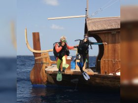 Two divers prepare to jump into the ocean from a beautifully crafted boat, showcasing the excitement of underwater adventures and scuba diving experiences.
