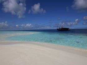 A serene view of a boat anchored in crystal-clear turquoise waters, surrounded by a pristine sandy beach — an ideal setting for relaxation and exploration.
