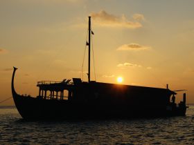 A stunning silhouette of a boat against a vibrant sunset, showcasing the vessel's elegant profile as it rests on calm waters.