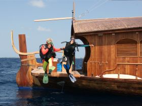 Two divers prepare to jump into the water from a beautifully crafted wooden boat, showcasing the excitement of underwater exploration and adventure.