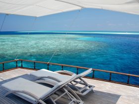 A serene view from the lounge area of a boat, showcasing comfortable seating overlooking stunning turquoise waters and coral reefs — perfect for relaxation and enjoying the scenery.