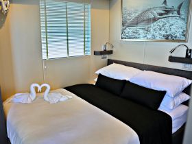 A cozy cabin interior featuring a neatly made bed with towel swans, perfect for romantic getaways on the water.