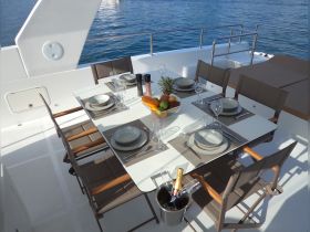 An elegant dining setup on a yacht featuring a beautifully arranged table with plates, glasses, and fresh fruit, perfect for onboard meals and gatherings.