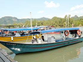 A vibrant boat is docked at the pier, showcasing its sleek design against a backdrop of lush greenery and mountains, perfect for exploring nearby waters.