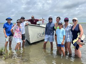 A cheerful group of friends and family poses by their boat, enjoying a fun day on the water — perfect for private charters and memorable outings.