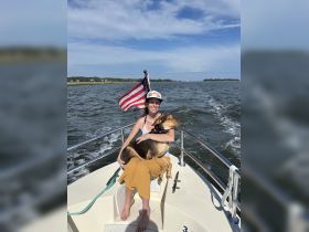 A joyful moment on the water as a woman enjoys a sunny day on a boat with her dog, showcasing the perfect blend of relaxation and adventure.