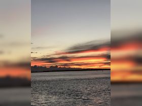 A stunning sunset over the water, showcasing vibrant colors and a serene coastline — perfect for capturing the beauty of nature during a boat trip.