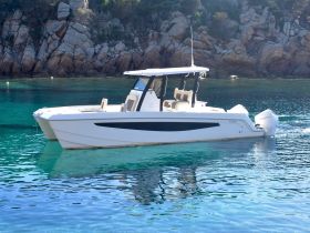 A sleek speedboat glides through crystal-clear waters, showcasing its elegant design against a stunning rocky backdrop.