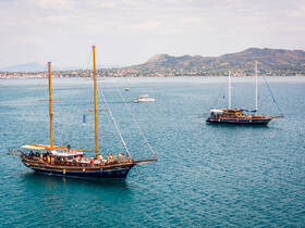 Two beautiful sailing boats are anchored in the serene waters, with groups of people enjoying the scenic views — perfect for a day of relaxation and adventure on the sea.