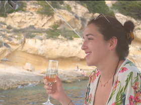 A woman enjoys a glass of champagne while relaxing on a boat, with a beautiful beach backdrop — perfect for celebrating special moments on the water.