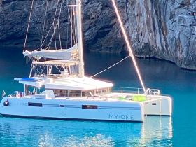 A stunning catamaran named 'MY-ONE' anchored in serene turquoise waters, surrounded by dramatic cliffs — perfect for a relaxing day on the water.