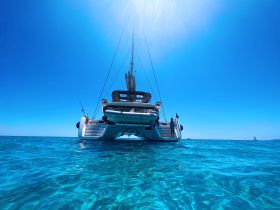 A stunning view of a catamaran sailing through crystal-clear waters, showcasing its sleek design against a bright blue sky.