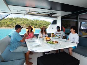 A cheerful group enjoys a meal together on a boat, surrounded by stunning turquoise waters — perfect for memorable dining experiences at sea.