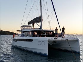 Two individuals stand on the deck of a sleek catamaran during sunset, showcasing a perfect moment for yacht enthusiasts and sunset cruises.