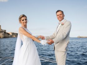 A joyful couple celebrates their wedding aboard a boat, capturing a romantic moment against a stunning waterfront backdrop.