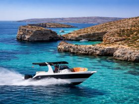 A sleek speedboat navigates the stunning turquoise waters along a picturesque coastline, showcasing the beauty of the surrounding cliffs and islands.