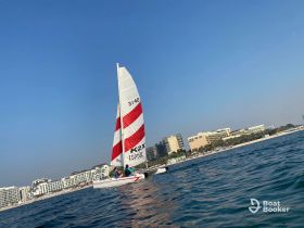 A vibrant catamaran sails along the coastline, showcasing a perfect day for water activities against a backdrop of beach resorts.
