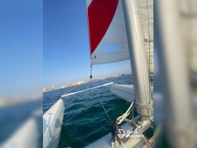 A close-up view of a sailboat's sail and rigging, showcasing the vessel in motion against a clear blue sky and calm waters.