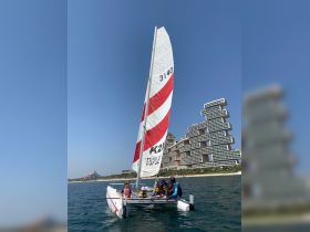 A group of children and adults enjoy a sailing experience on a catamaran, showcasing the fun of water activities in a vibrant coastal setting.