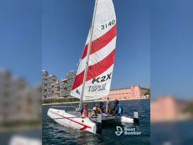 A group of children and an instructor enjoy a sailing experience on a catamaran, surrounded by stunning waterfront views — perfect for family adventures on the water.