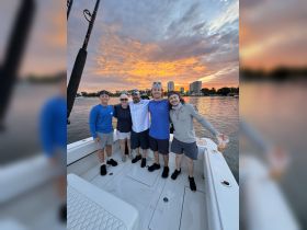 A cheerful group of friends poses together on a boat at sunset, capturing a memorable moment during their outing on the water.