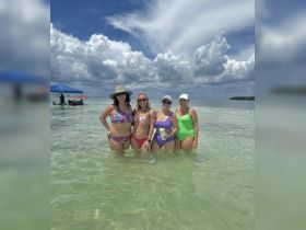 A joyful group of friends enjoys a sunny day at the beach, wading in the shallow waters — perfect for summer fun and memorable celebrations.