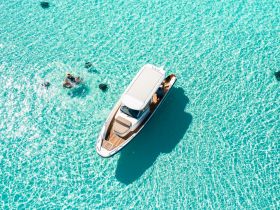 An aerial view captures a stunning scene of a boat anchored in crystal-clear turquoise waters, with a person enjoying the water nearby — a perfect representation of a tropical getaway.