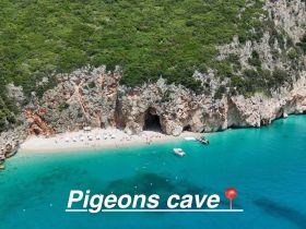 A stunning aerial view of Pigeons Cave, showcasing a beautiful beach with visitors enjoying the turquoise waters — a perfect destination for boat tours and exploration.