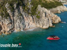 A stunning aerial view of Couple Bay, showcasing a vibrant boat near a picturesque beach with people enjoying the sun and water — perfect for a day of relaxation and adventure.