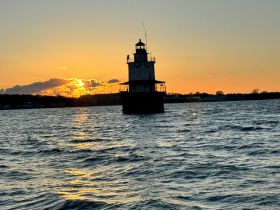 A stunning sunset behind a lighthouse, casting a warm glow over the water — a picturesque moment perfect for capturing the beauty of coastal landscapes.