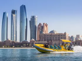 A vibrant speedboat named 'The Yellow Boats' glides through the waters of Abu Dhabi, showcasing the stunning skyline and architectural marvels in the background — perfect for city tours and sightseeing adventures.