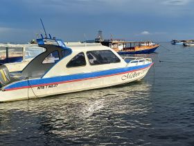 A sleek speedboat named 'Melben' docked in calm waters, showcasing its design against a backdrop of other boats and a clear sky.