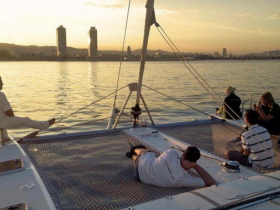 A group of friends relaxes on a catamaran during a stunning sunset, enjoying the serene waters and beautiful skyline — perfect for a memorable evening on the water.