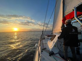 A sailor navigates a yacht during a stunning sunset, capturing the beauty of the ocean and the thrill of sailing.