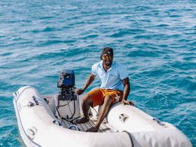 A smiling individual enjoys a ride on a small boat in clear blue waters, showcasing the vibrant atmosphere of a boating adventure.