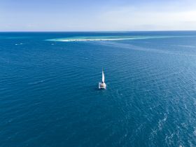 A stunning aerial view of a sailboat navigating through deep blue waters, showcasing the beauty of sailing adventures in open seas.