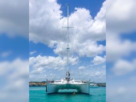 A stunning view of a catamaran anchored in clear turquoise waters, showcasing its sleek design against a backdrop of fluffy clouds and distant shoreline.