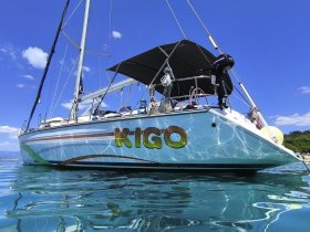 A stunning view of the KIGO yacht gliding through crystal-clear waters, showcasing its sleek design and vibrant colors under a bright blue sky.