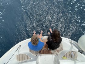 A couple enjoys a serene moment on the edge of a boat, dipping their feet in the ocean — a perfect snapshot of relaxation and connection on the water.