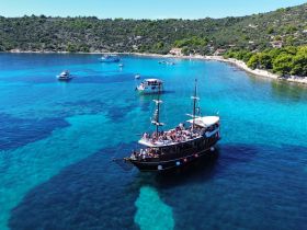 An aerial view of a vibrant bay filled with boats, showcasing a lively group enjoying their time on a classic vessel amidst stunning turquoise waters.