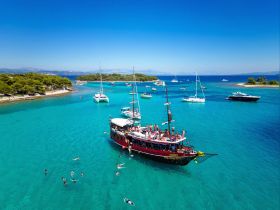 A vibrant scene of guests enjoying a sunny day on the water, swimming around a lively boat in stunning turquoise waters — perfect for summer adventures and group outings.