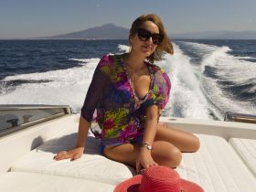 A stylish woman enjoys a sunny day on a boat, with stunning ocean views and a glimpse of a distant mountain, perfect for showcasing the joy of boating adventures.