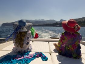 Two women enjoy a sunny day on a boat, taking in the beautiful coastal scenery — a perfect moment for relaxation and adventure on the water.