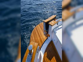 A close-up view of a beautifully crafted wooden deck on a boat, showcasing the elegant design and sparkling blue waters in the background — perfect for nautical enthusiasts.