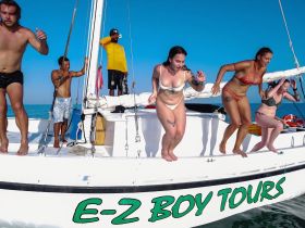 A lively group of friends jumps off the side of a boat, enjoying a fun day on the water with E-Z Boy Tours — perfect for adventure seekers and party lovers.