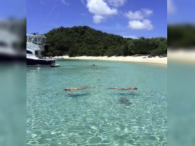 Two friends float peacefully in the crystal-clear waters of a secluded beach, with a boat anchored nearby — a perfect scene for relaxation and fun in the sun.