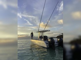 A man stands on the bow of a fishing boat during a stunning sunset, capturing the essence of adventure on the water.