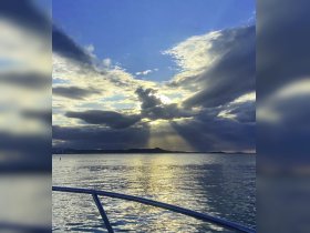 A stunning view of the sunset over calm waters, captured from the bow of a boat, showcasing the beautiful interplay of light and clouds.