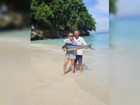 A couple proudly displays their catch of the day on a beautiful beach, celebrating a successful fishing trip in paradise.