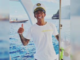 A cheerful boat captain gives a thumbs up while standing on deck, showcasing the beautiful ocean backdrop — perfect for a day of adventure on the water.